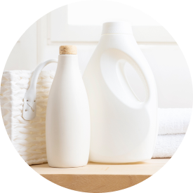  Bottles of laundry detergent and fabric softener on a wooden surface with towels and a basket in the background.