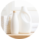  Bottles of laundry detergent and fabric softener on a wooden surface with towels and a basket in the background.