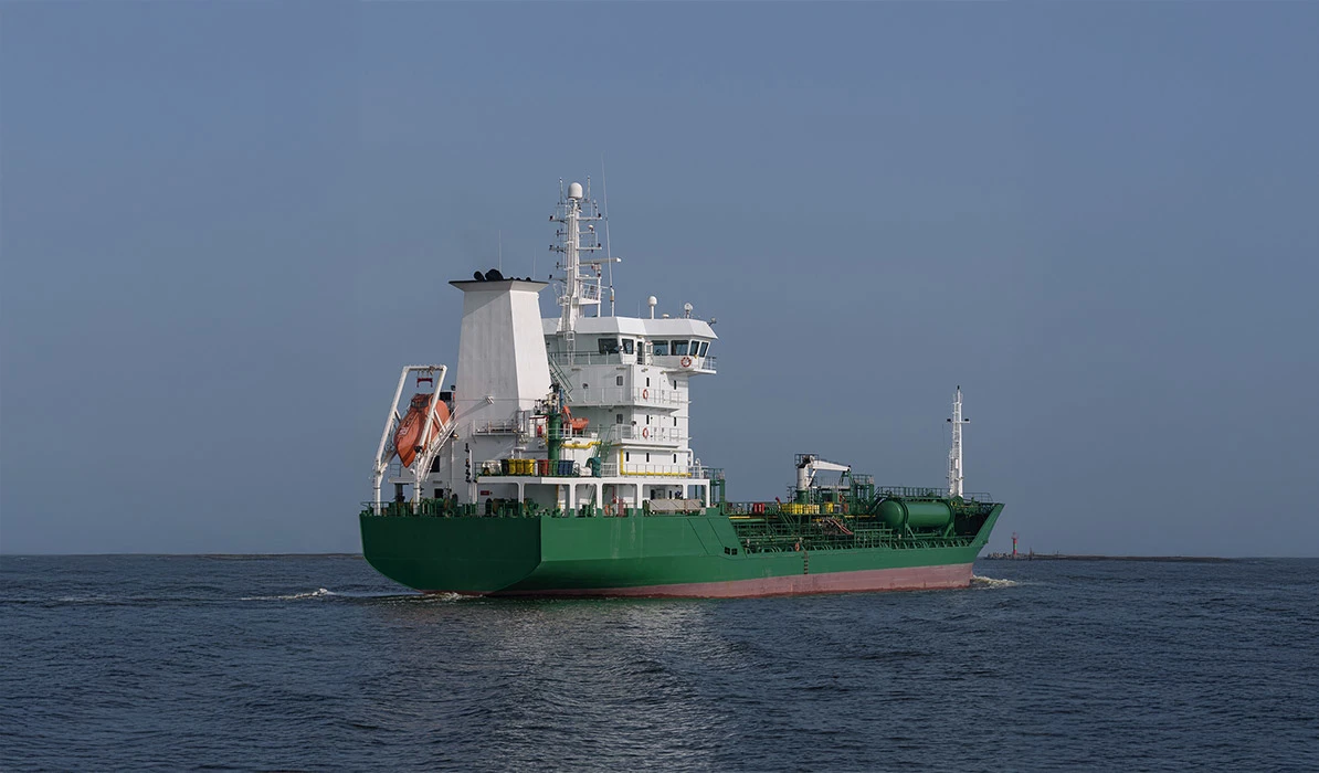 A green cargo ship sailing on calm blue waters under a clear sky.