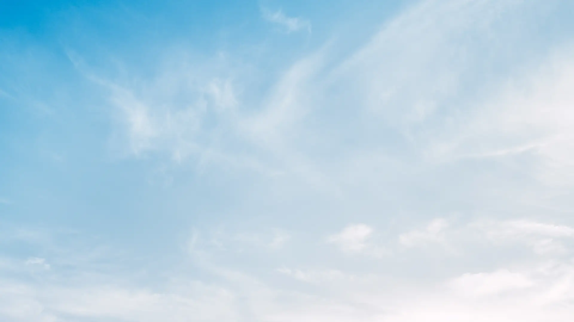 Clouds gracefully drift across a bright blue sky.