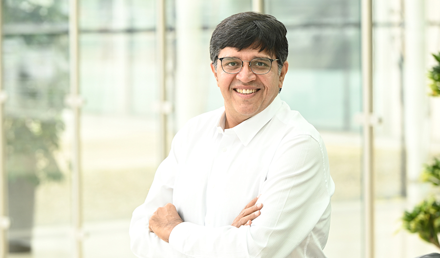 Man with glasses wearing a white shirt, smiling outdoors with office building in the background.