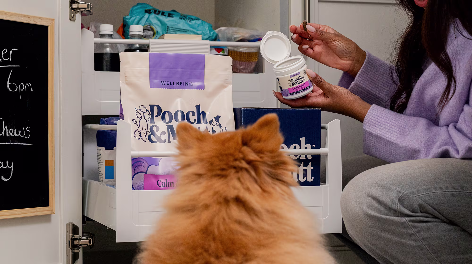 A fluffy dog faces away from us as they watch their owner get out a Pooch & Mutt Hemp Chew.