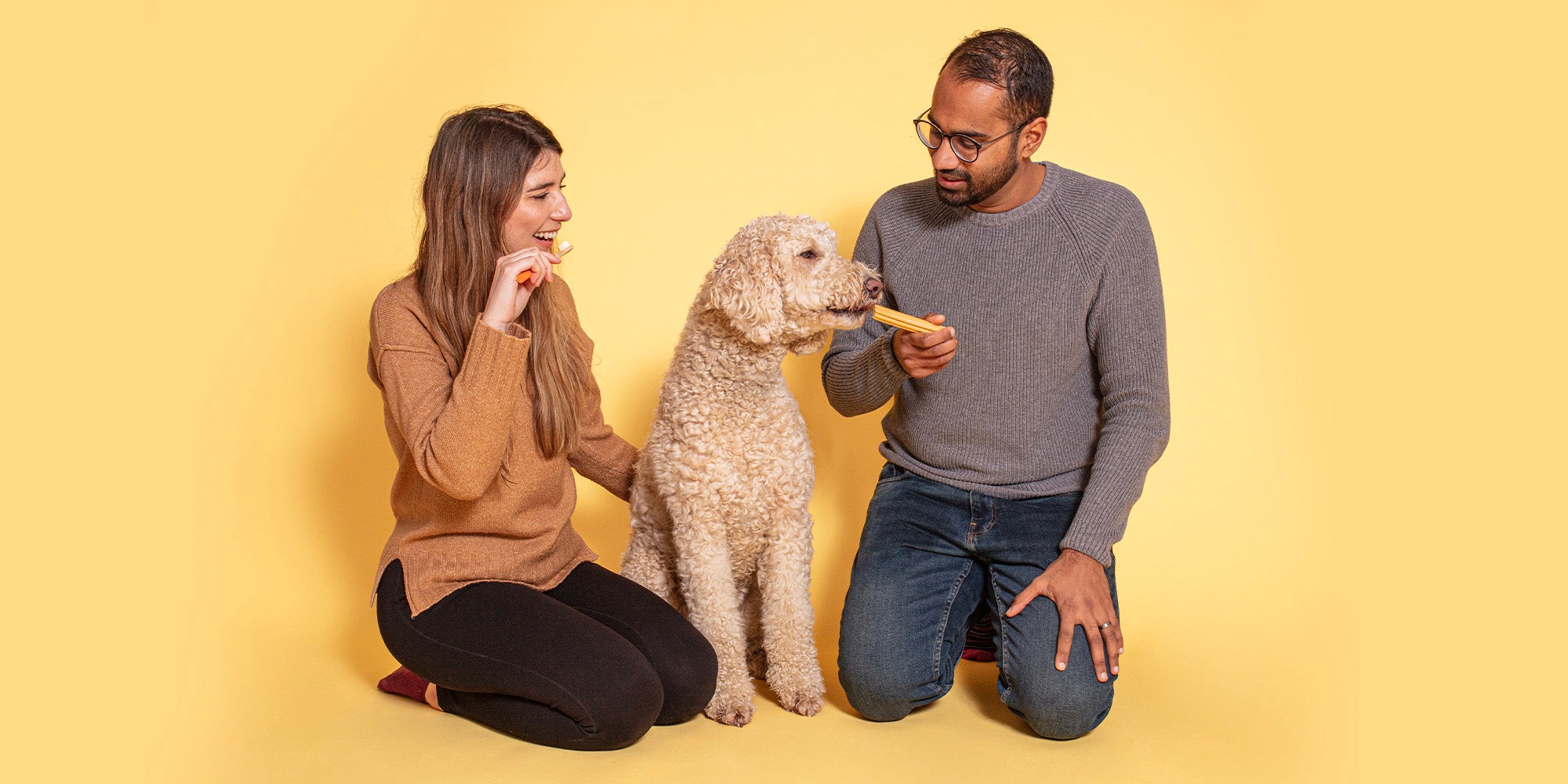 A man and woman with their golden coloured dog, against a pale orange background