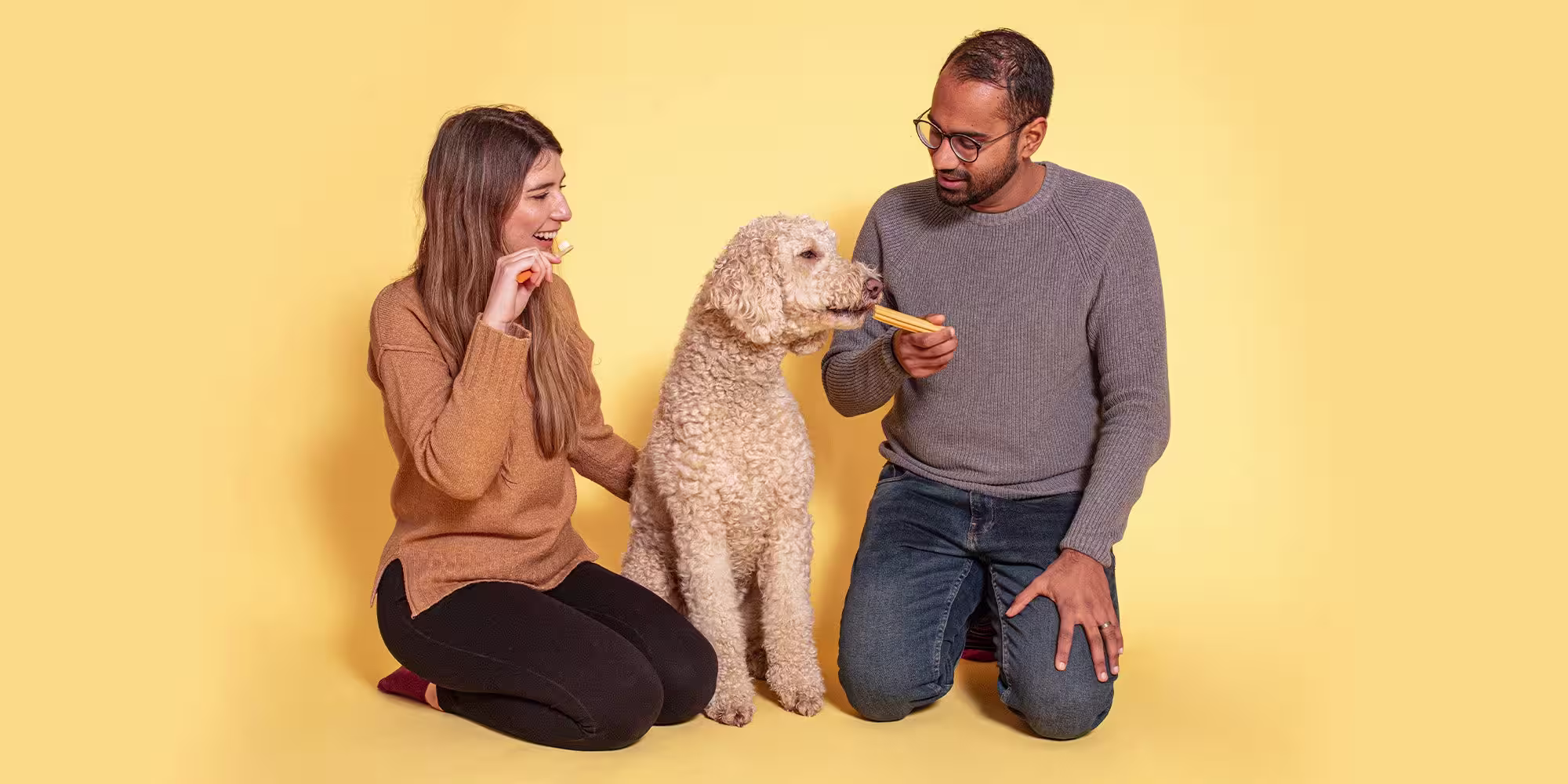 A man and woman with their golden coloured dog, against a pale orange background