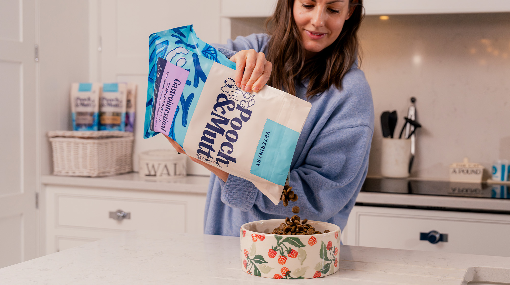 A dog owner standing in their kitchen whilst pouring some Pooch & Mutt Gastrointestinal Dry Food from their Veterinary range into a dog bowl.