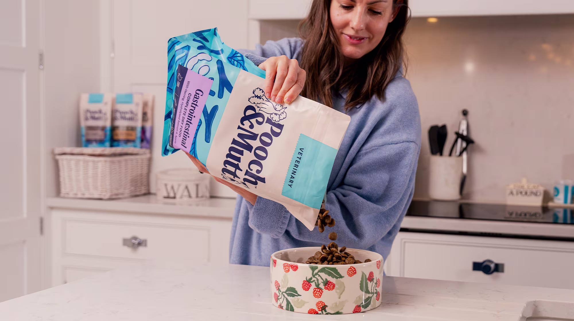 A dog owner standing in their kitchen whilst pouring some Pooch & Mutt Gastrointestinal Dry Food from their Veterinary range into a dog bowl.