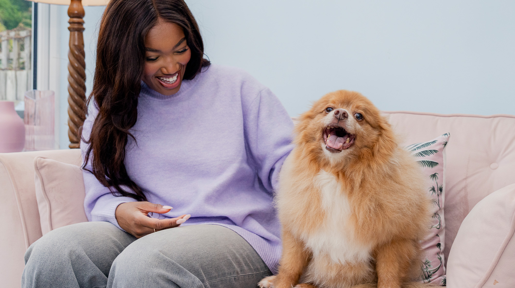 A dog owner sits on their sofa with their dog who is showing their teeth like they're smiling.