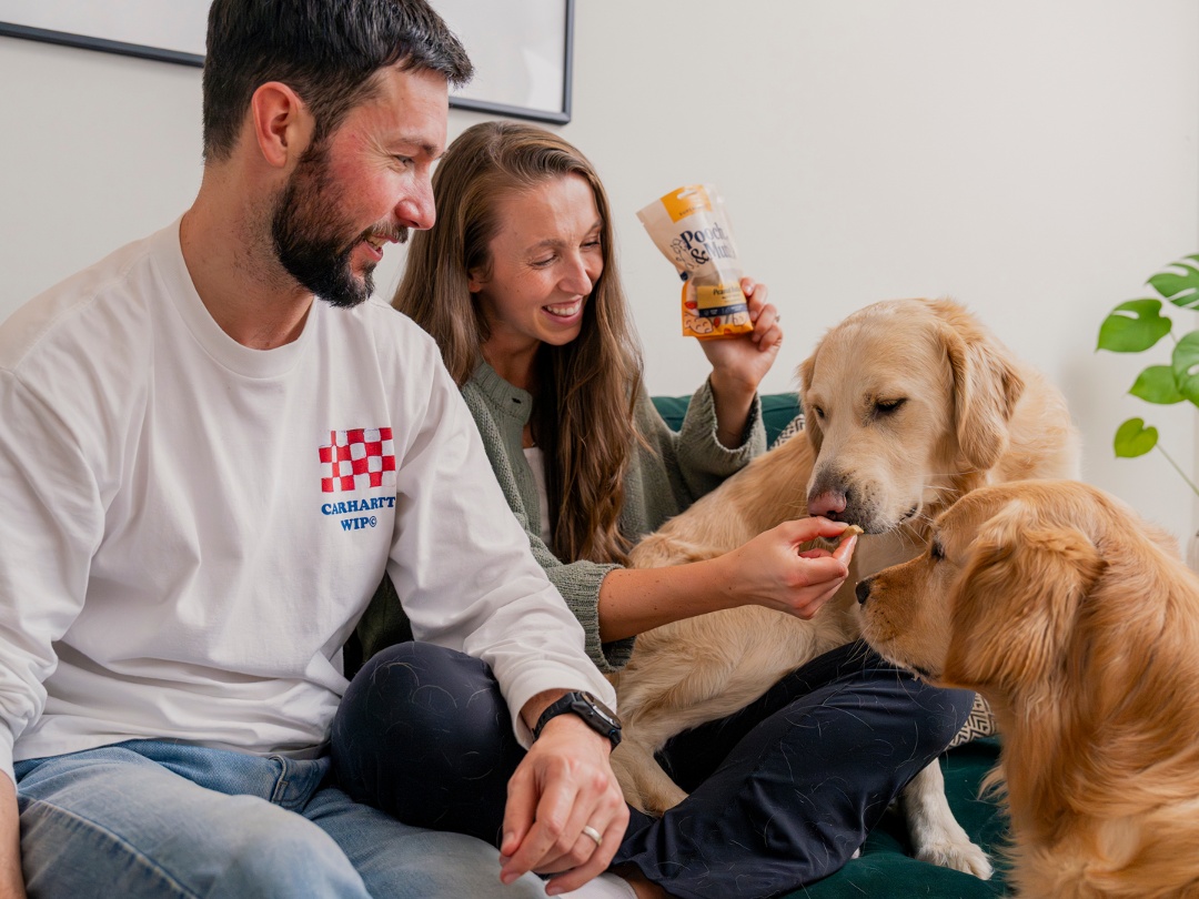 A man and woman feed their dog treats