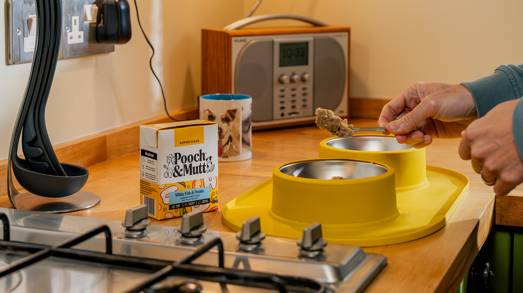A dog owner spoons Pooch & Mutt Wet Food into a yellow dog bowl