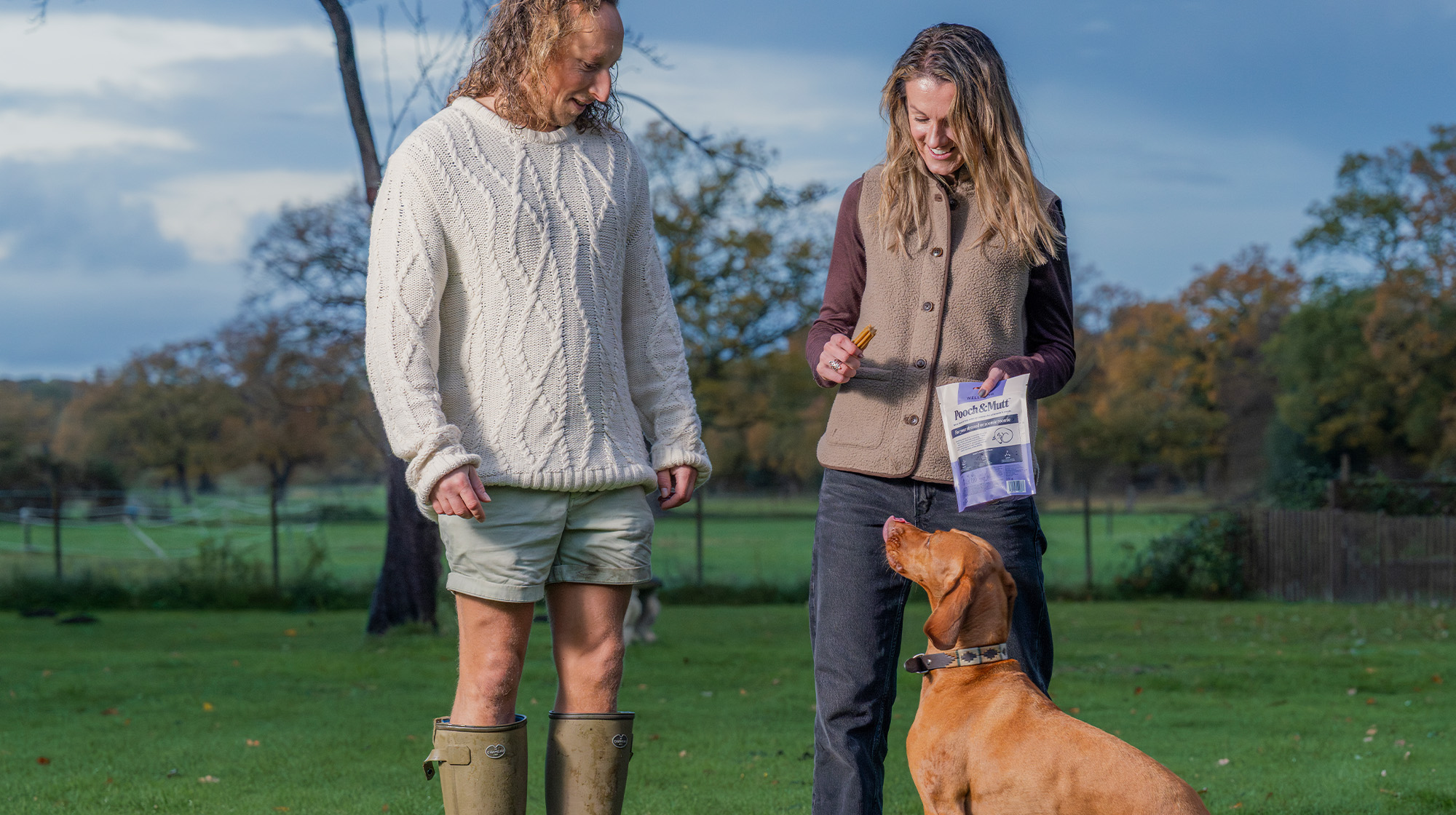 Two dog owners stand outside with their auburn Pointer staring up at them.
