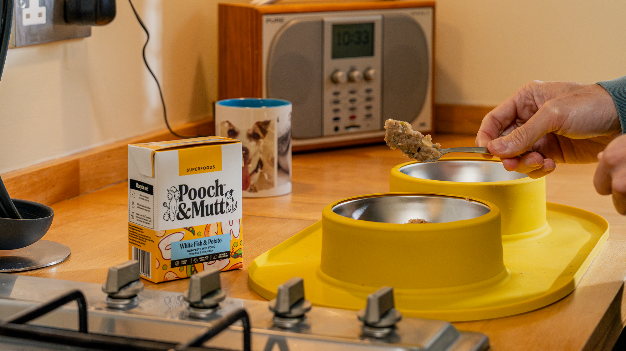 A shot of a dog owner's hand as they spoon Pooch & Mutt's White Fish & Potato Wet Food into yellow dog food bowls.
