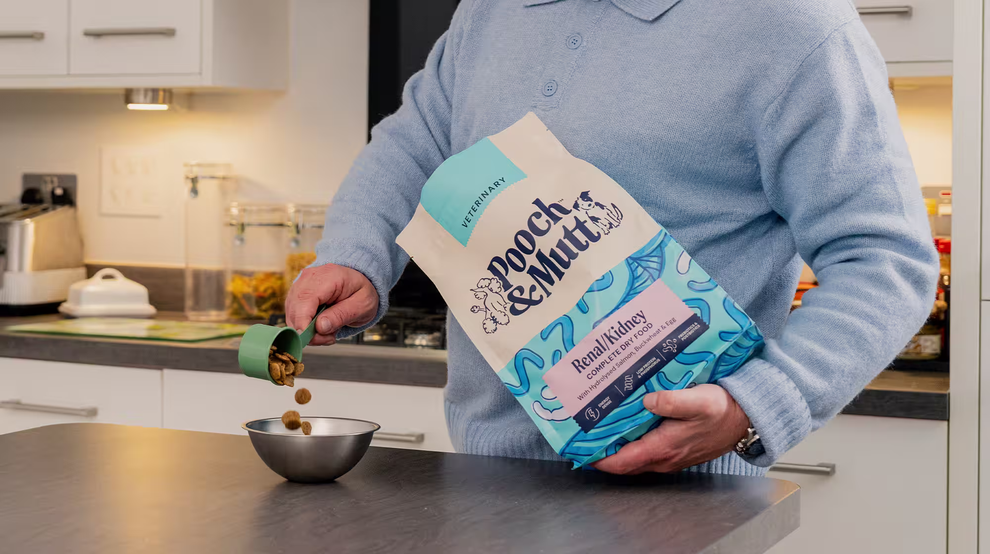 A dog owner holding a pack of Pooch & Mutt's Renal Dry Food as he pours some into a dog bowl.