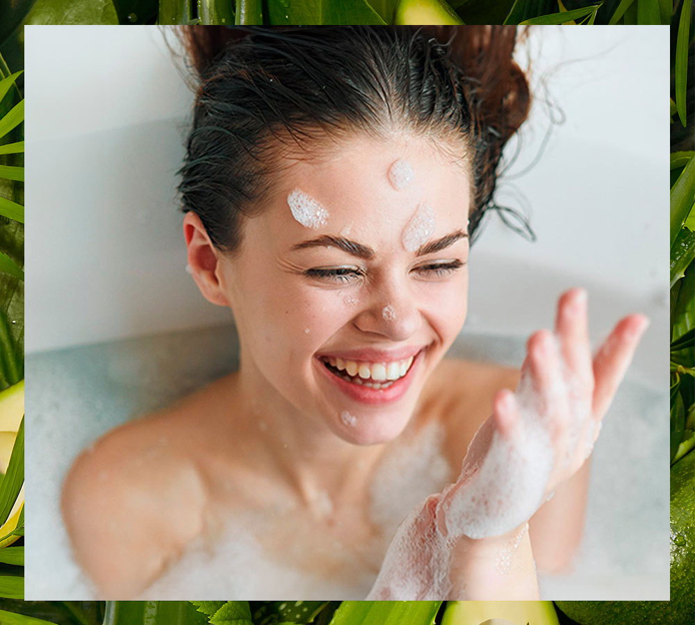 Mujer con pelo oscuro en bañera, riendo, espuma en la cara.
