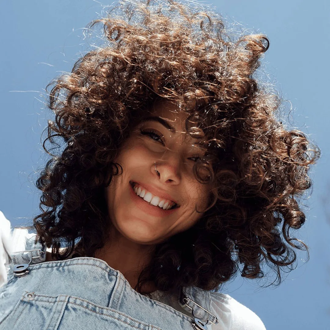 Un retrato de mujer joven con una sonrisa en su rostro sosteniendo su cabello dañado en un moño