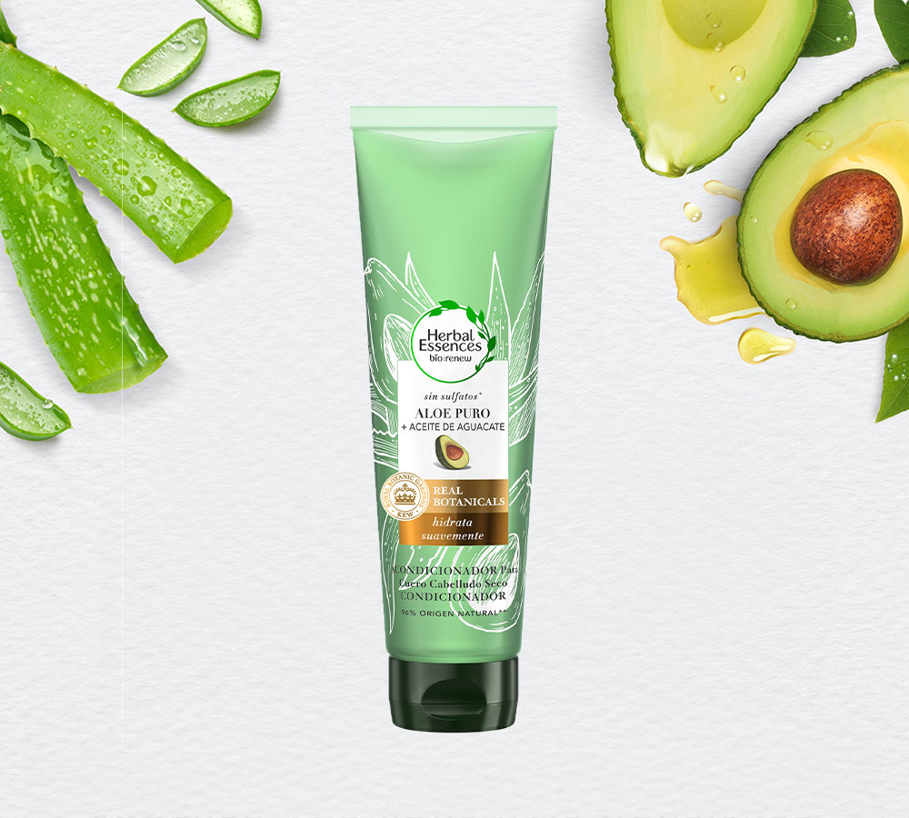 Tubo verde claro de Acondicionador Herbal Essences Aloe Puro + Aceite De Aguacate, rodeado de hojas de aloe y aguacate en rodajas.
