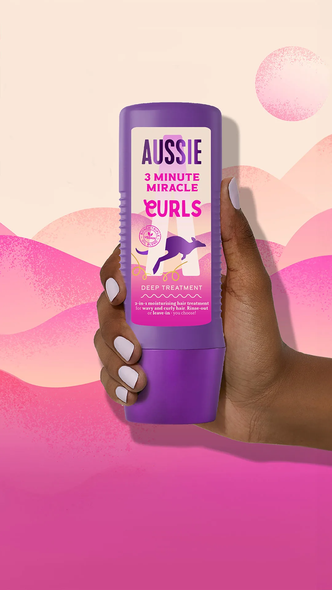 Mano sostiene botella morada de Aussie 3 Minute Miracle Tratamiento Rizos sobre fondo ondulado rosa y naranja.