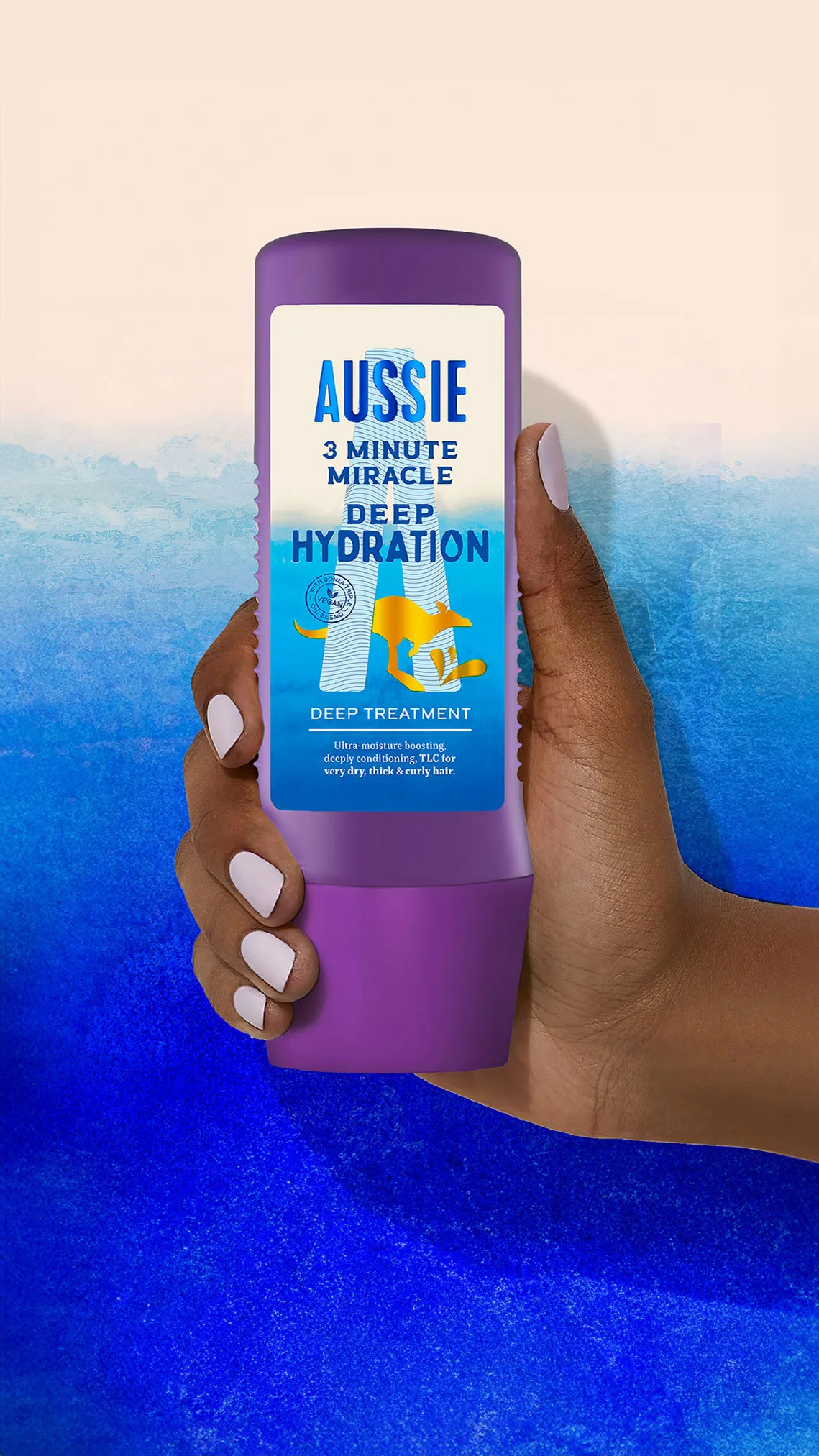 Una mano sostiene una botella morada de Aussie 3 Minute Miracle Hidratación Profunda Mascarilla, con fondo azul y blanco.