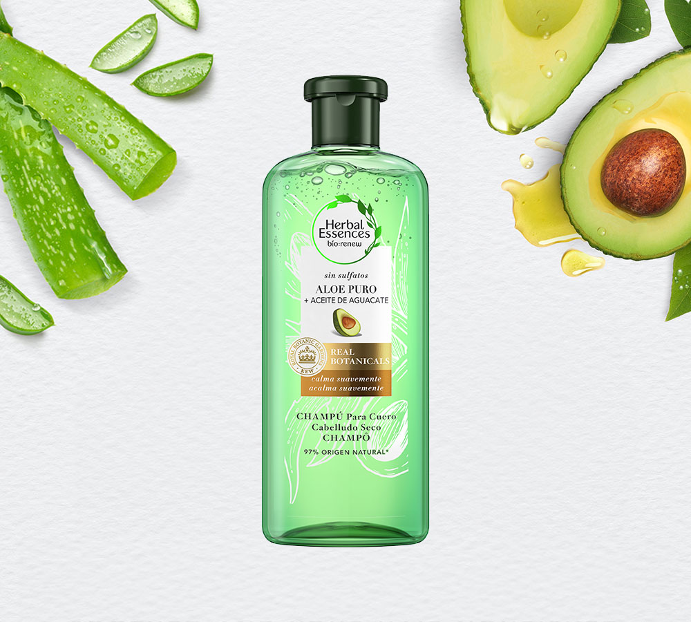 Tubo verde claro de Champú Herbal Essences Aloe Puro + Aceite De Aguacate, rodeado de hojas de aloe y aguacate en rodajas.
