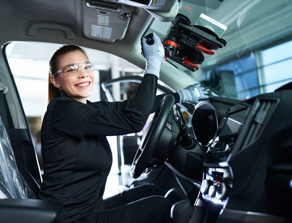Technicienne souriante dans une voiture remplacant un parebrise