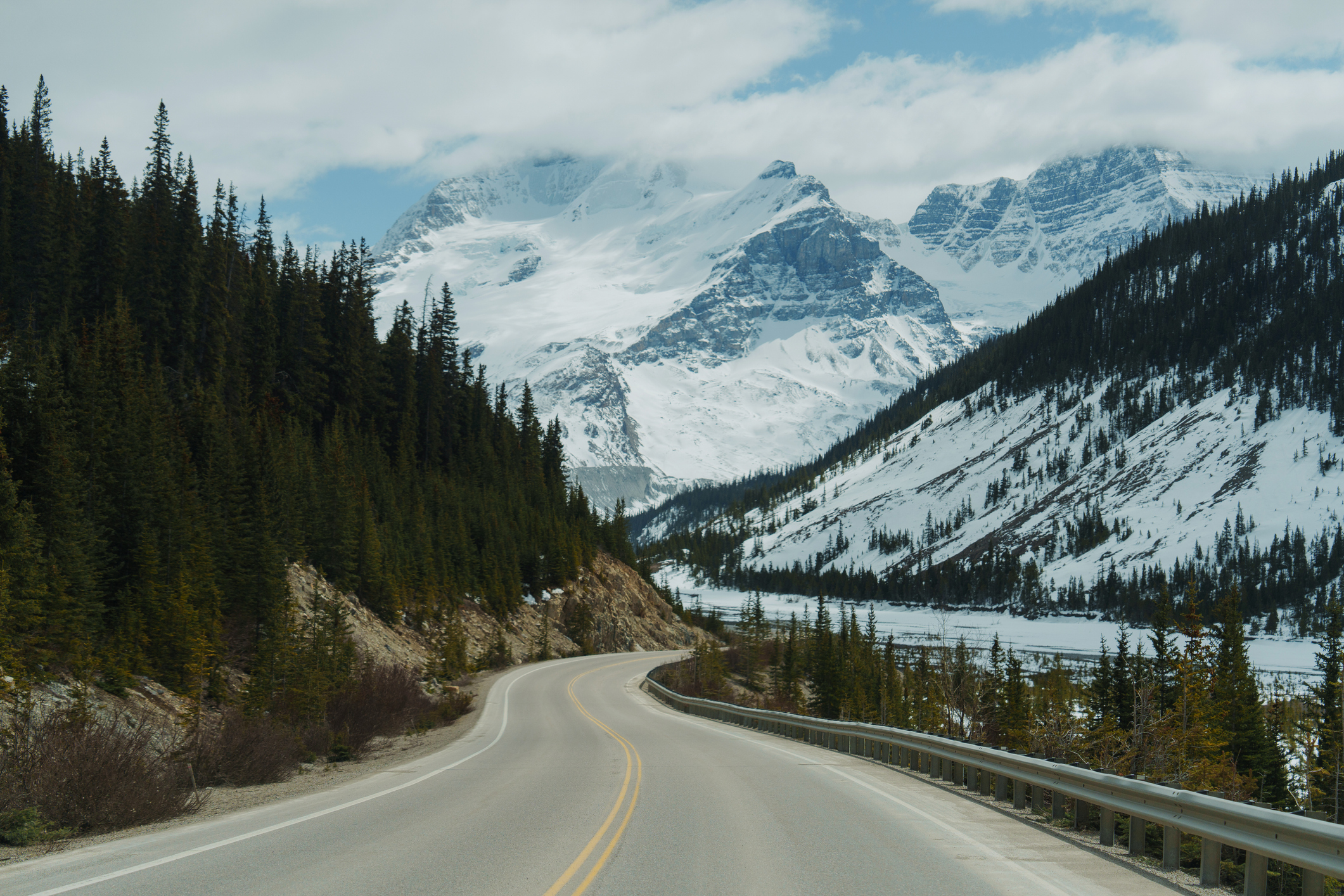A winding road through a snowy valley, with mountains in the background.