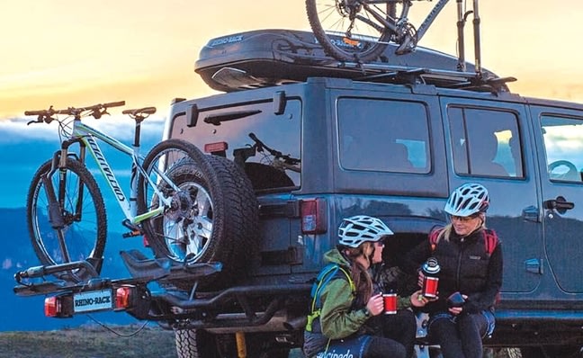 Two people beside a car carrying a bicycle on the roof and at the rear