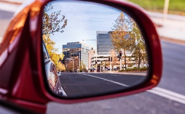 Car side mirror showing a city reflected in it