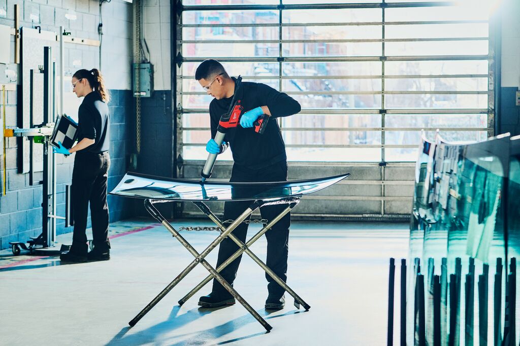 Two people in a workshop adding glue to a windshield