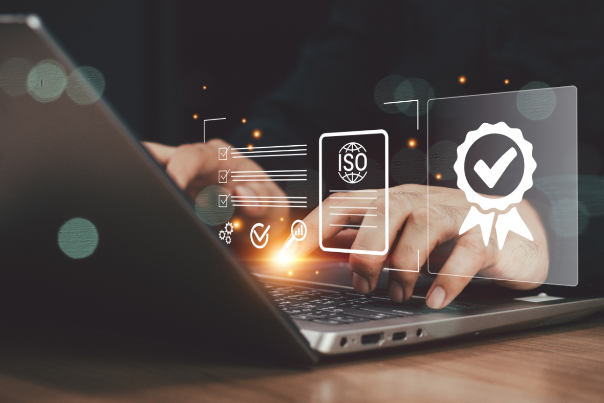 Hands typing on a laptop keyboard with digital icons of certification, a checkmark ribbon, and an ISO document overlayed, representing quality standards and compliance.