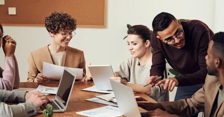 A group of coworkers with their laptops on a conference table.