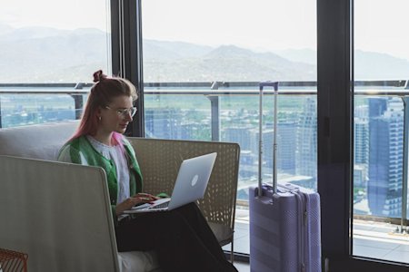 A person sitting in a tall building next to their suitcase while using Splashtop Remote Access on their computer to work remotely while traveling.