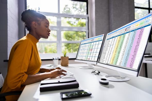 Woman using two screens to review giant spreadsheet