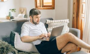 A man sitting on a couch while working from home with a laptop in his lap.