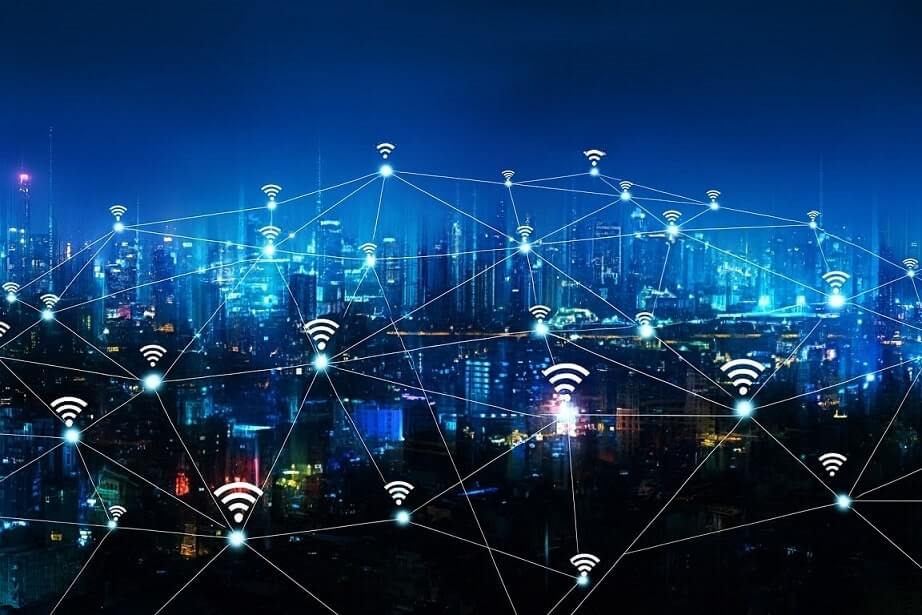 A city skyline at night with glowing lines and Wi-Fi symbols connecting buildings, representing a networked or smart city with widespread wireless internet connectivity.