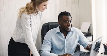 Two coworkers viewing a laptop screen and smiling.