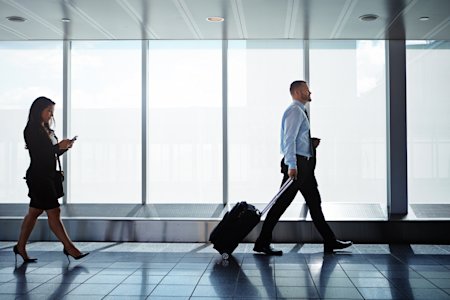 Business professionals walking through an airport terminal, illustrating the impact of rising business travel costs.