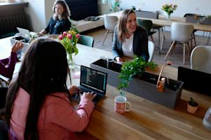 A group of women sitting at a conference desk in the office on their laptops.