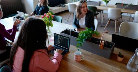 A group of women sitting at a conference desk in the office on their laptops.