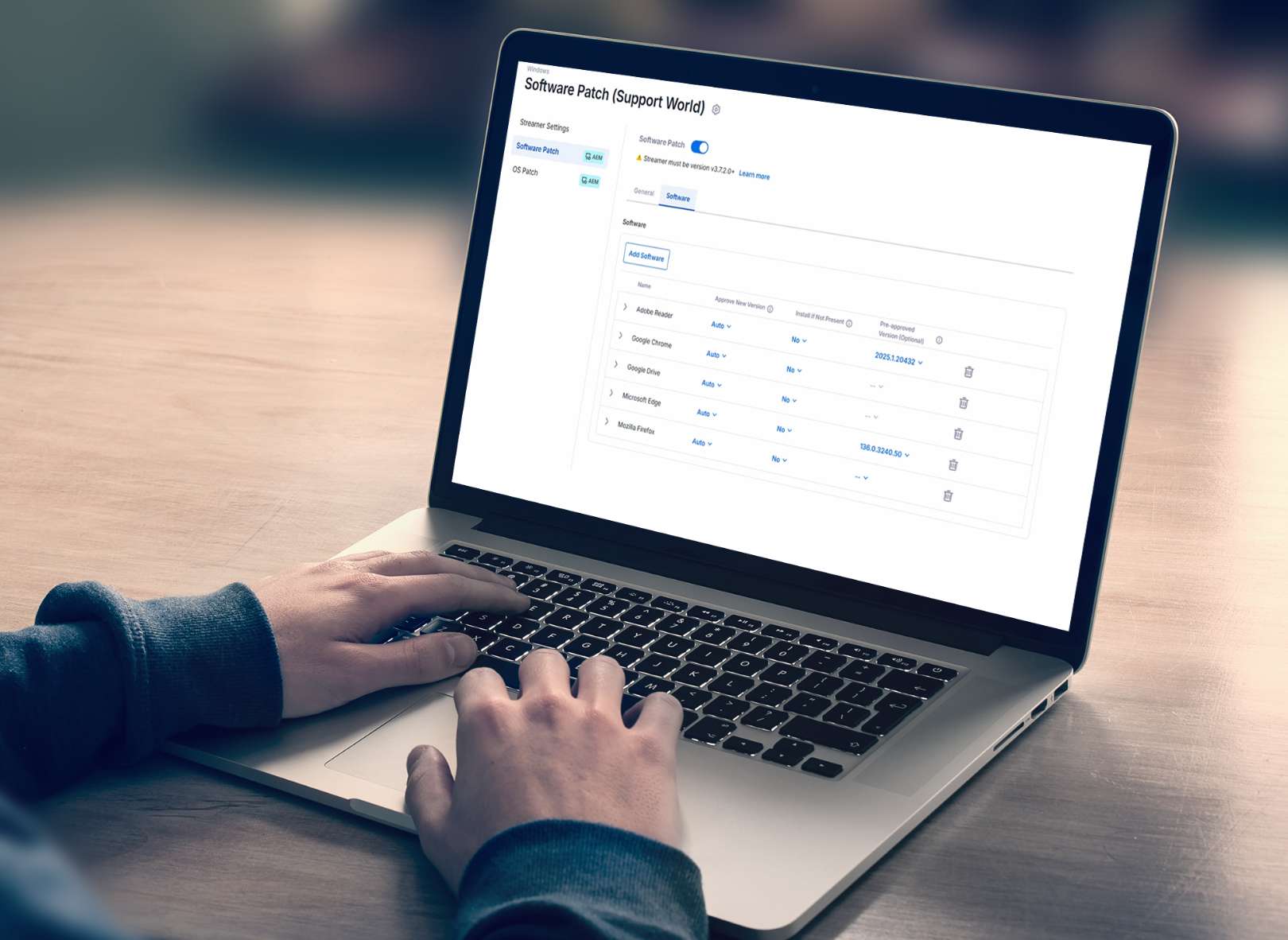 A person using a laptop displaying a software management dashboard with a list of tasks, including status, due dates, and actions, on a wooden table.