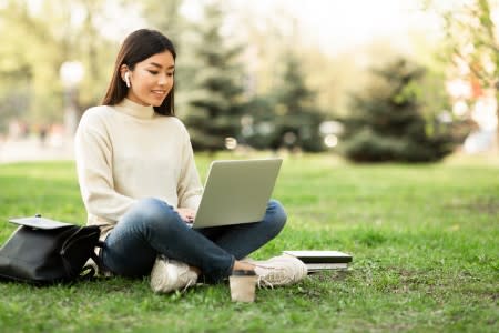 Female student is seen sitting outdoors, engrossed in an article about distance remote learning with Splashtop