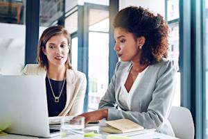 Two businesswomen collaborating on a laptop during an IT risk assessment meeting in a modern office.