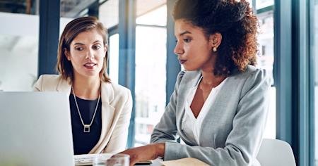 Two businesswomen collaborating on a laptop during an IT risk assessment meeting in a modern office.