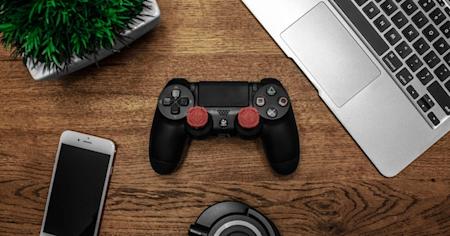 A gaming controller, laptop, and mobile device on a desk.