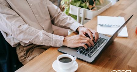 Person working remotely on a laptop at a wooden table with a coffee cup and notebook, symbolizing remote work trends in 2025.
