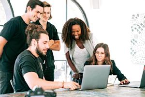 A group of works standing around a desk looking at a laptop.