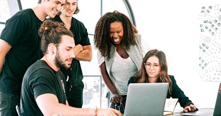 A group of works standing around a desk looking at a laptop.