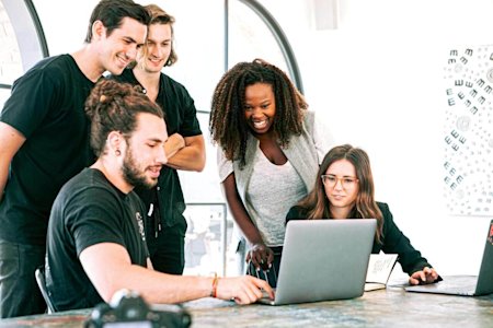 A group of works standing around a desk looking at a laptop.