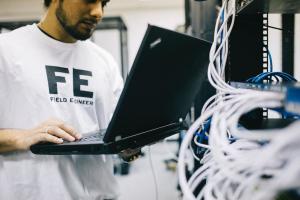 A field service technician working on a laptop near wires.