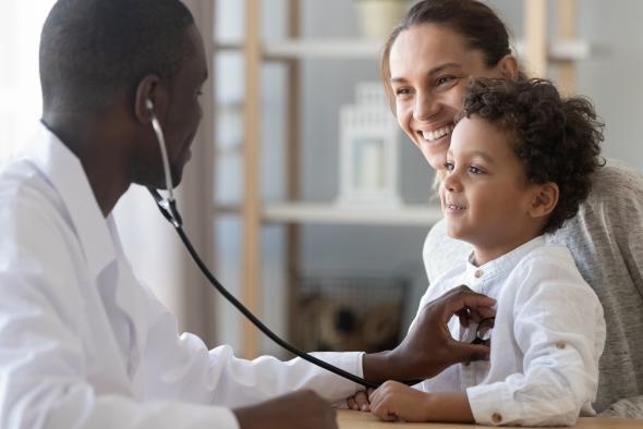 A doctor is examining a young boy, that is being held by his smiling mother.