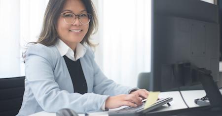 A woman smiling while working on her computer in an office.