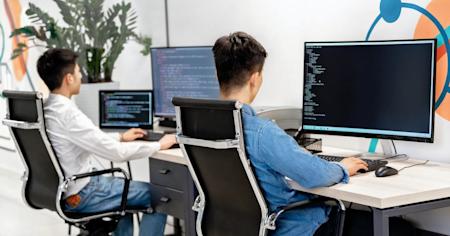 Two people working on their computers at their adjoining desks.